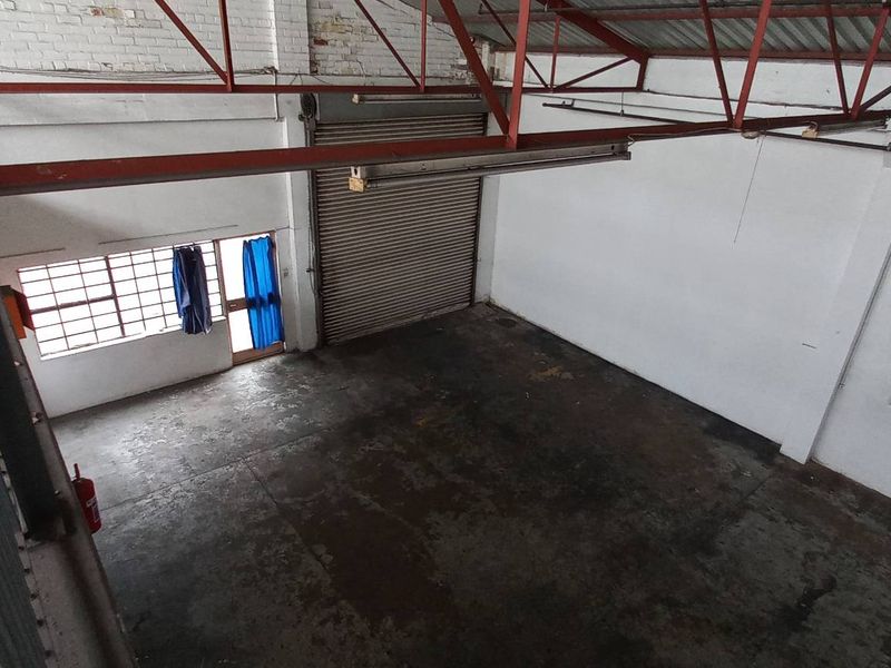 Spacious industrial warehouse unit featuring high ceilings with exposed steel trusses, a roller shutter door, and a mezzanine level overlooking the main floor area.
