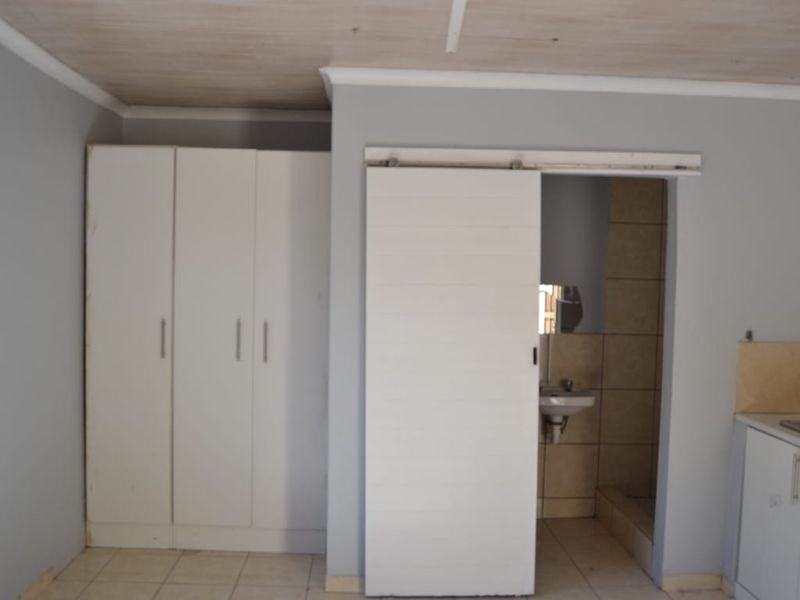 Open plan living area featuring built-in cupboards, a sliding door leading to a bathroom, and basic kitchen cabinetry with tiled flooring.