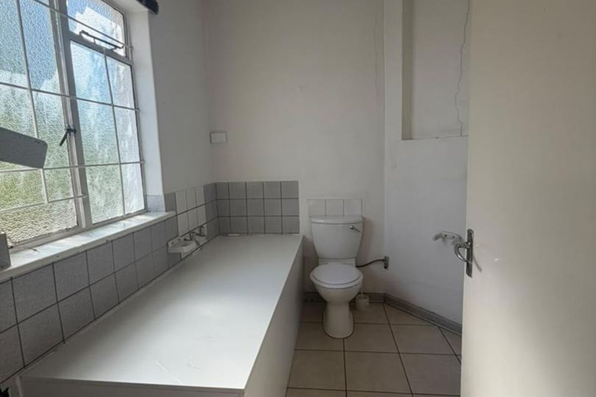 A functional bathroom featuring a built-in bathtub, toilet, and tiled finishes, currently vacant and ready for renovation or cosmetic updates.
