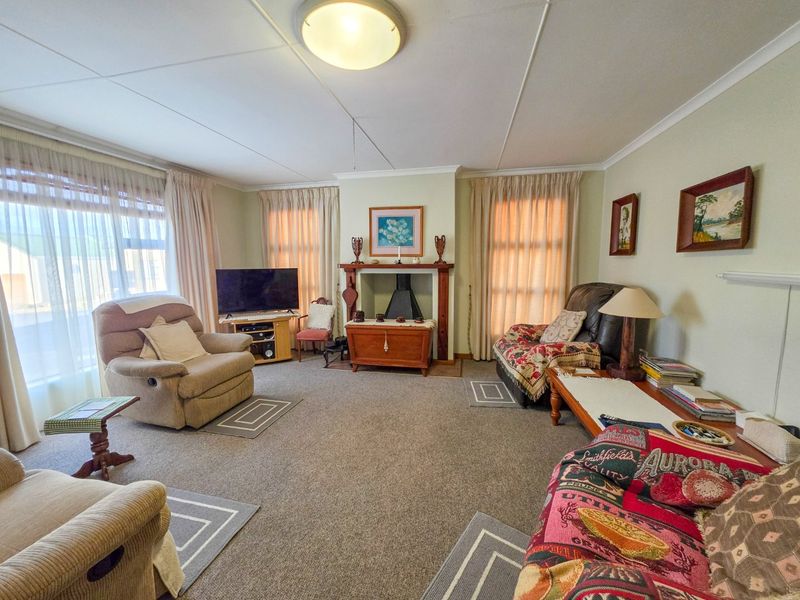 A spacious living room featuring a central fireplace with a mantelpiece, neutral wall tones, and carpeted flooring, offering a comfortable and traditional living space.