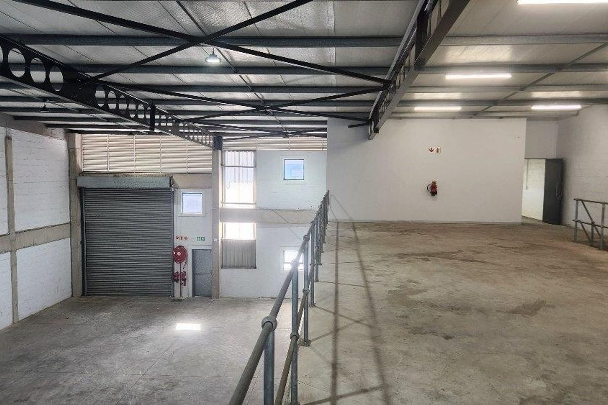 Spacious industrial utility area featuring a mezzanine level, high steel truss ceilings, roller shutter door access, and concrete flooring suitable for storage or operations.