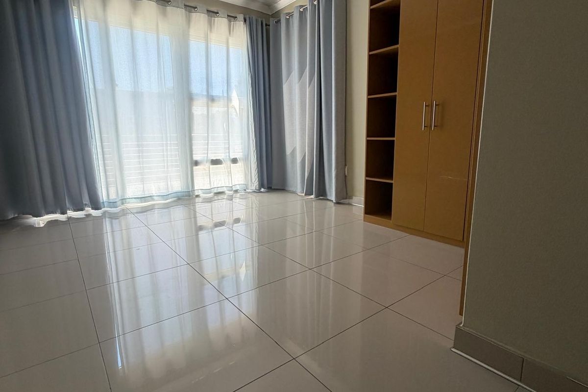 A bright, empty bedroom featuring polished tiled flooring, built-in wooden cupboards, and a large sliding glass door providing natural light.