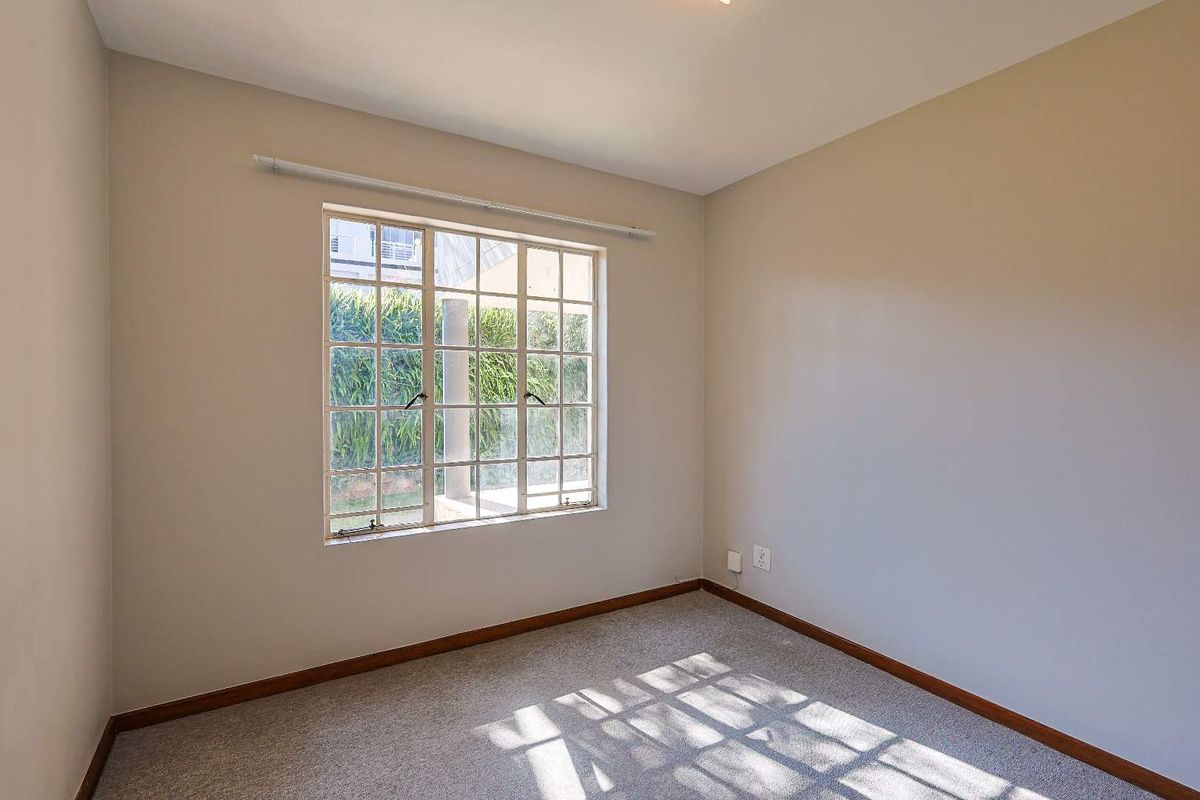 A bright, empty bedroom featuring neutral walls, carpeted flooring, and a large multi-pane window allowing for natural light.
