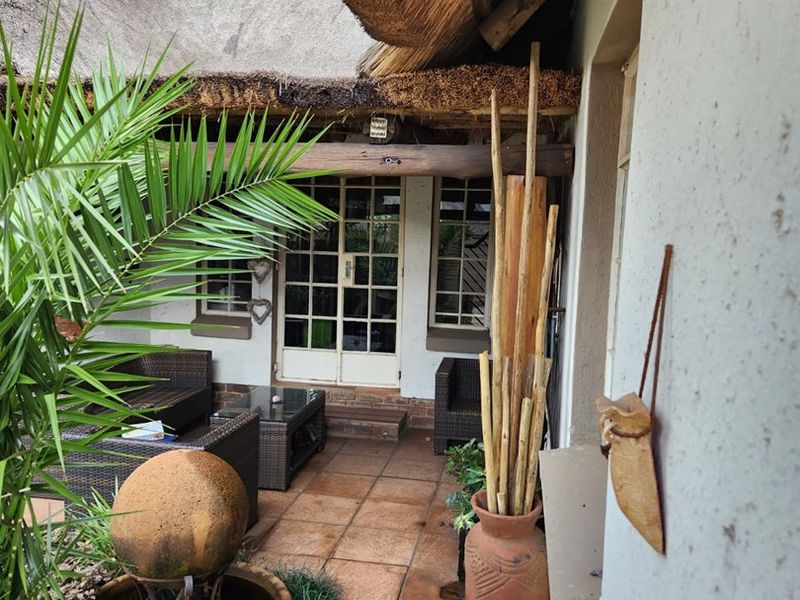 A covered patio area featuring a traditional thatched roof, tiled flooring, and direct access to the home through classic french doors.