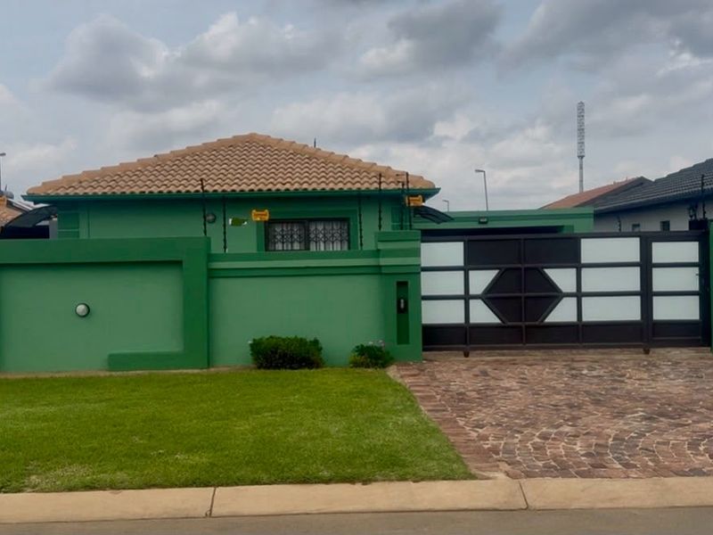 Front exterior view of a residential property featuring a paved driveway, secure sliding gate, and perimeter wall with electric fencing.