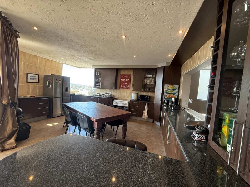 Spacious kitchen featuring dark wood cabinetry, granite countertops, tiled backsplash, and recessed lighting, with an integrated dining area and views.