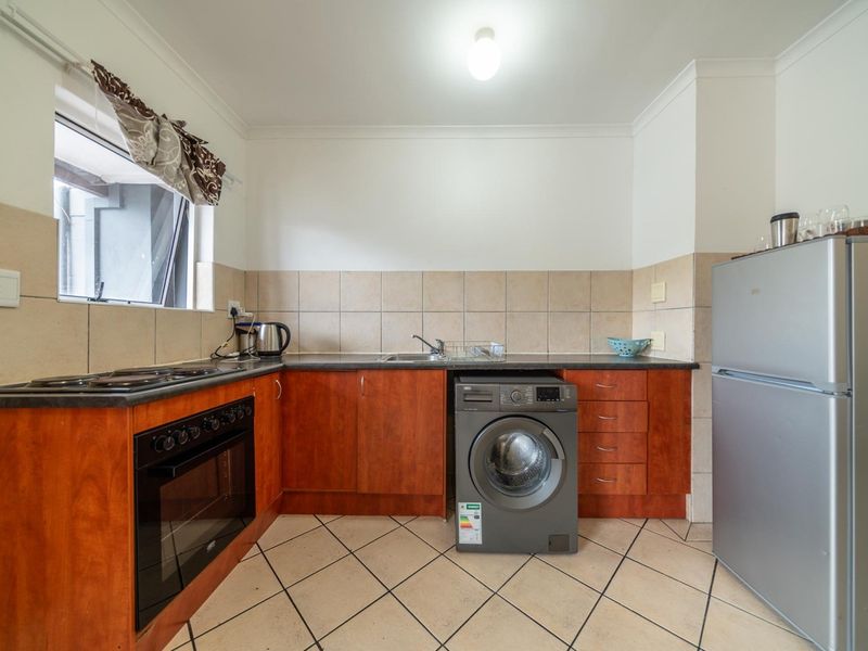 A functional kitchen featuring wood-finish cabinetry, tiled backsplash, tiled flooring, and integrated appliances including an oven and hob.