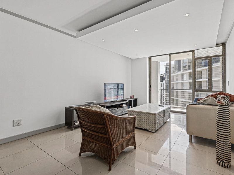 A bright living room featuring tiled flooring, recessed ceiling lighting, and large sliding glass doors leading to a balcony.
