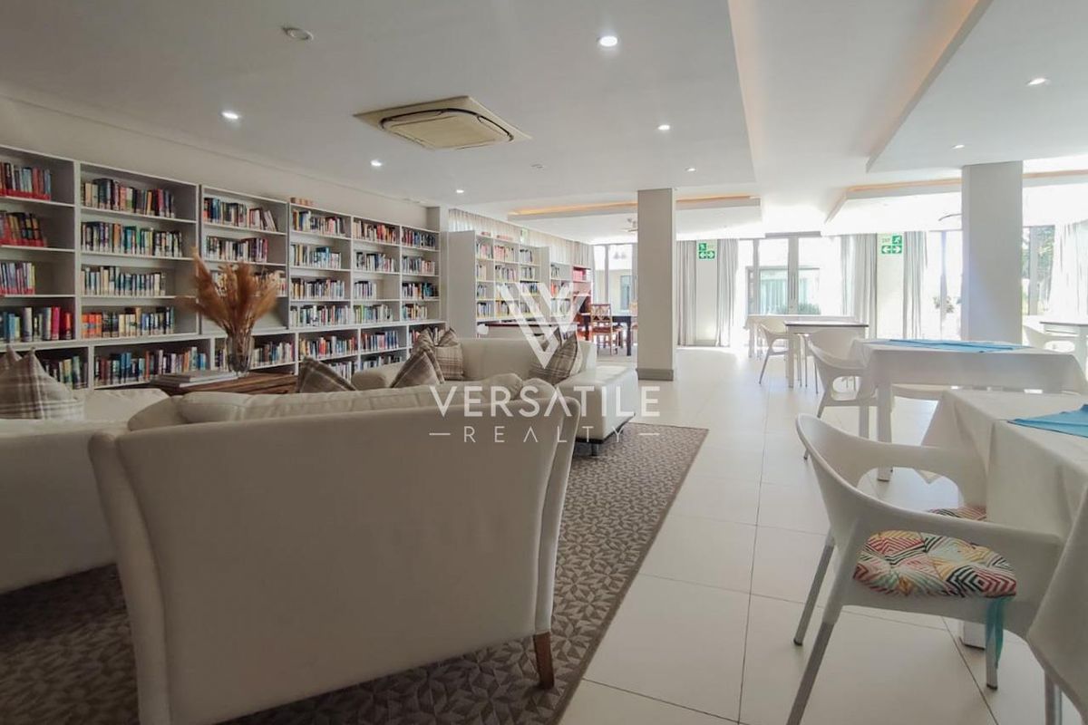 Spacious communal lounge and library area featuring extensive built-in shelving, recessed ceiling lighting, and tiled flooring within a retirement village setting.