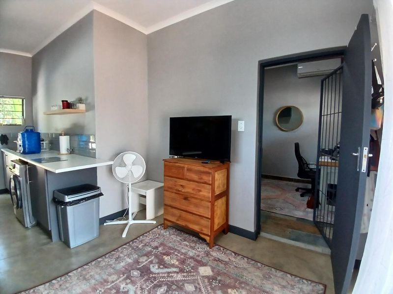 Open plan living area featuring polished concrete floors, a compact kitchen workspace, and a security gate leading to an adjacent room.
