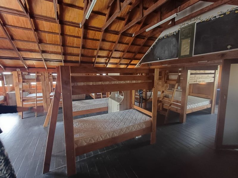 Spacious dormitory-style bedroom featuring exposed timber roof trusses, plywood ceiling, and dark timber flooring, providing a rustic and functional accommodation space.