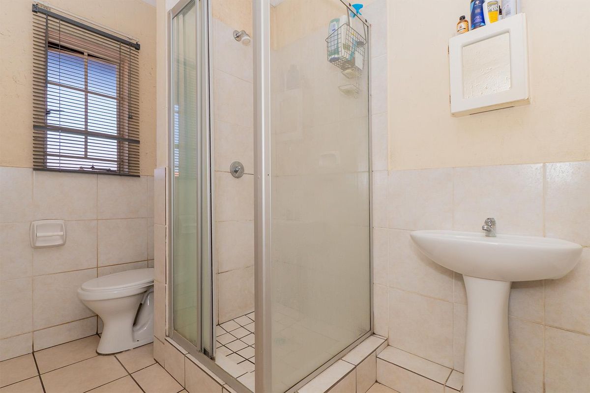 A functional bathroom featuring a glass-enclosed shower, pedestal basin, and toilet, finished with neutral wall and floor tiling.