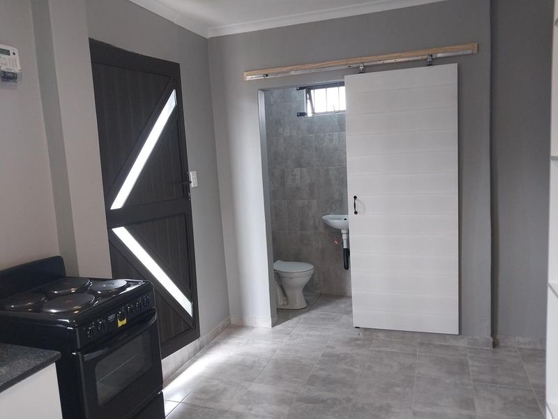 Kitchen area featuring tiled flooring, a freestanding stove, and a sliding barn door leading to an adjacent bathroom with a pedestal basin and toilet.