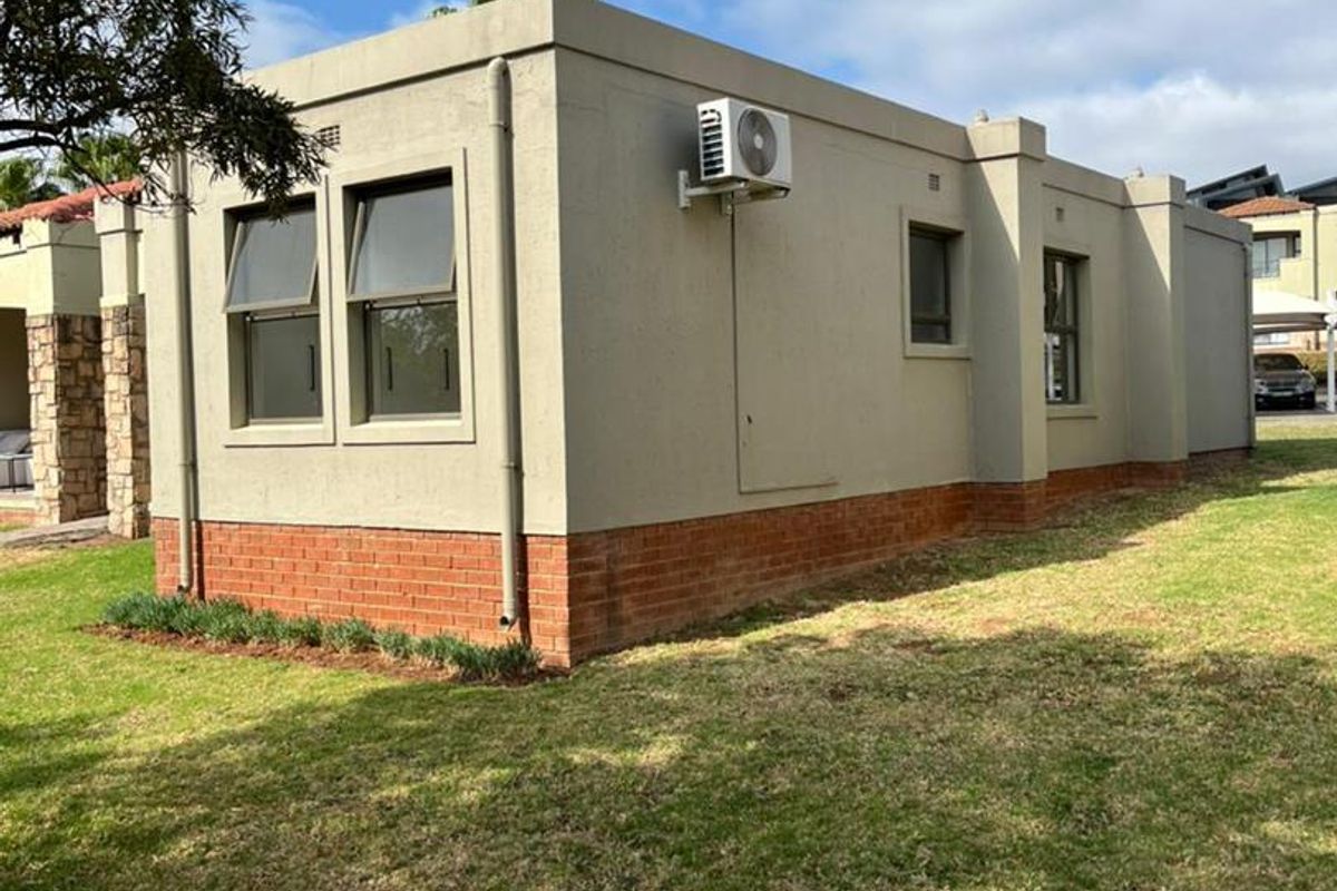 A view of the rear exterior elevation of the cluster home, featuring a brick plinth, casement windows, and an external air conditioning unit.