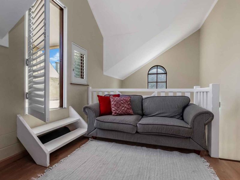 A cozy living area featuring vaulted ceilings, timber flooring, an arched window, and direct access to an outdoor space via a shuttered door.
