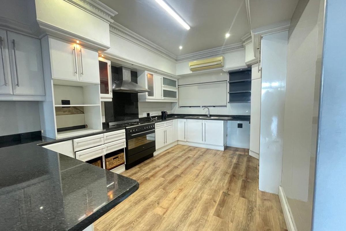 A spacious, well-maintained kitchen featuring white cabinetry, dark granite countertops, integrated appliances, and durable laminate flooring with modern crown molding details.