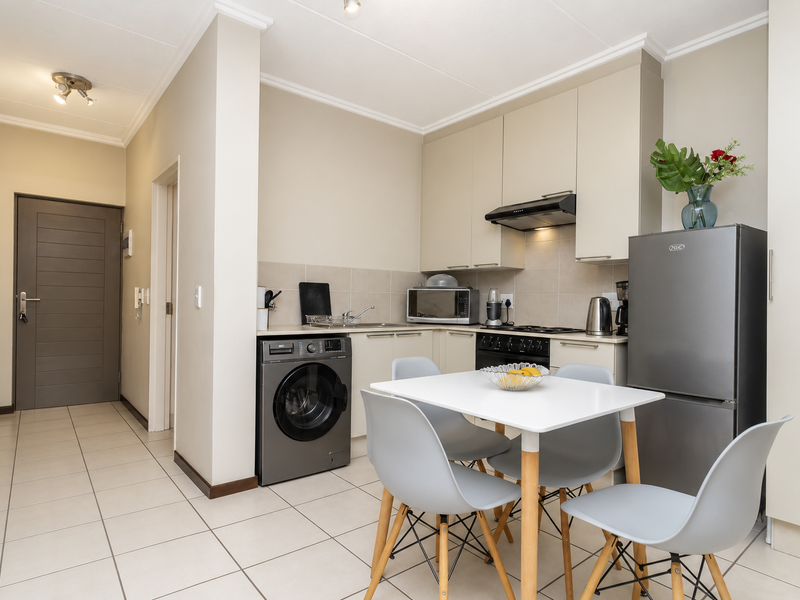 A modern open-plan kitchen area featuring neutral cabinetry, integrated appliances, tiled flooring, and a seamless transition to the apartment entrance hallway.