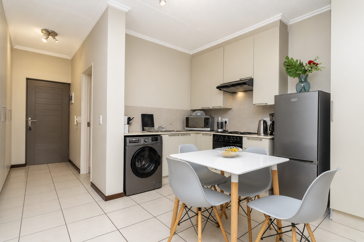 A modern open-plan kitchen area featuring neutral cabinetry, integrated appliances, tiled flooring, and a seamless transition to the apartment entrance hallway.