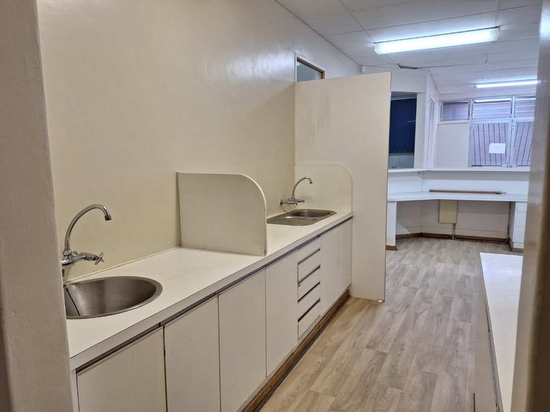 A functional office kitchenette featuring dual stainless steel sinks, ample laminate cabinetry, and durable vinyl flooring, providing a clean and practical workspace utility area.