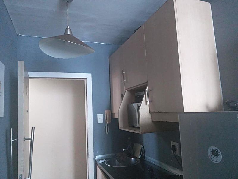 A compact kitchen area featuring built-in cabinetry, a sink, and a pendant light fixture, showing signs of wear and dated finishes.