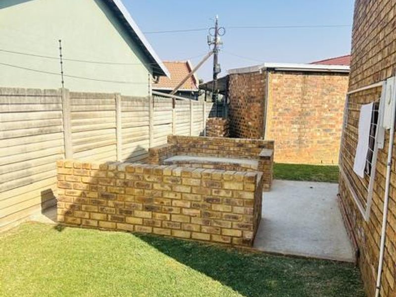 Rear garden area featuring a concrete patio, built-in brick seating, and a lawn enclosed by brick boundary walls with electric fencing.