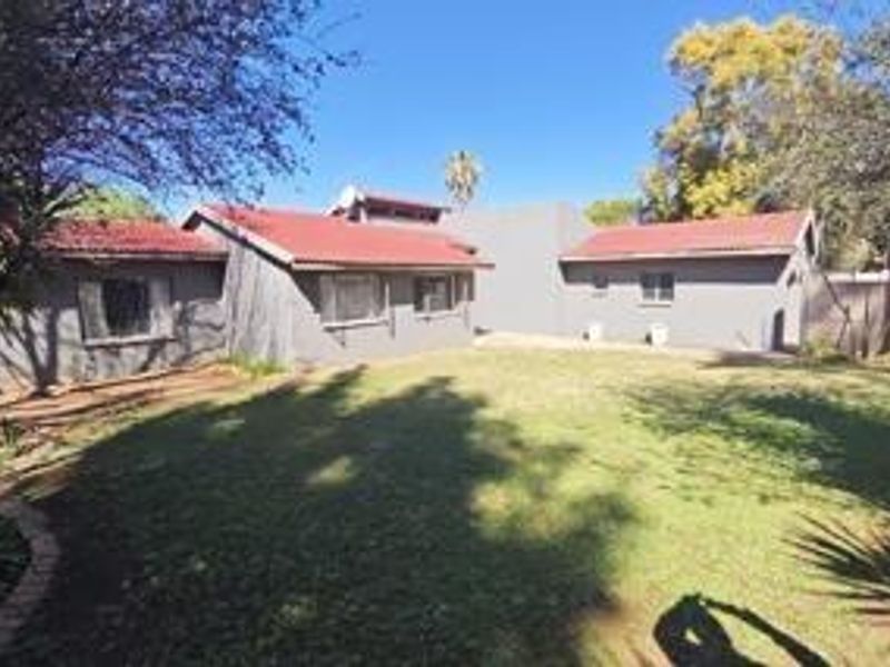 A view of the rear exterior of the house featuring a tiled roof, grey brick walls, and a spacious lawn area.