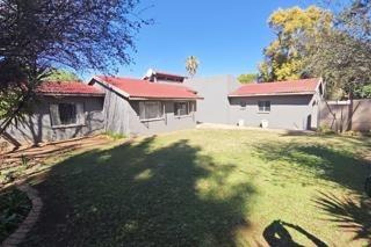 A view of the rear exterior of the house featuring a tiled roof, grey brick walls, and a spacious lawn area.