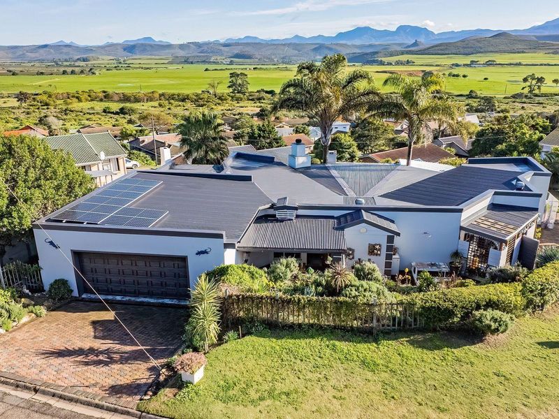 Aerial view of a modern residential property featuring a metal roof with solar panels, a paved driveway, double garage, and expansive rural landscape views.