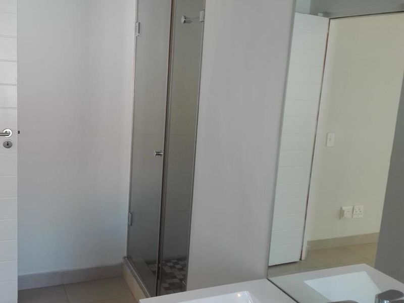 A clean, modern bathroom featuring a vanity basin with a mixer tap, a large wall mirror, and a glass-enclosed shower.