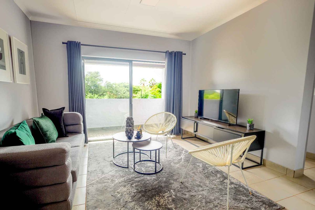 A bright and modern living room featuring tiled flooring and a large sliding glass door that opens onto a private balcony.