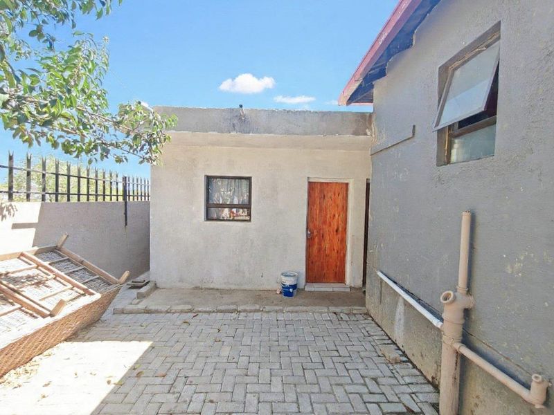 A rear courtyard area featuring paved flooring, perimeter walling with security spikes, and access to the main structure via a timber door.