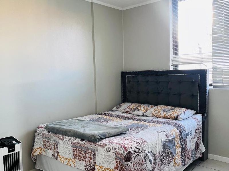 A functional bedroom featuring neutral wall tones, tiled flooring, and a window fitted with venetian blinds, providing a clean and simple living space.