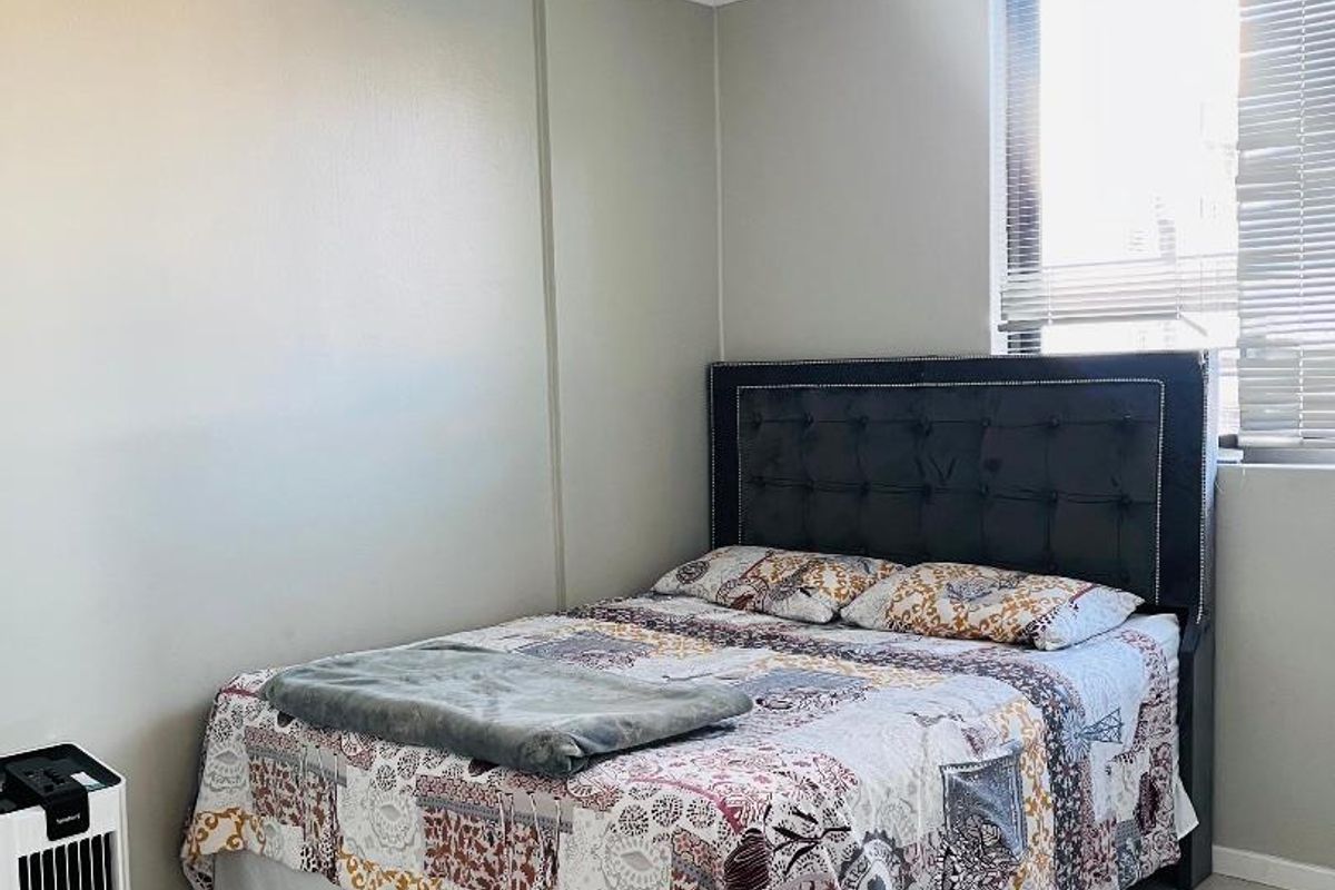 A functional bedroom featuring neutral wall tones, tiled flooring, and a window fitted with venetian blinds, providing a clean and simple living space.