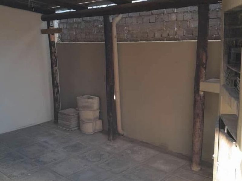 Covered outdoor patio area featuring a built-in braai, tiled flooring, and timber structural supports, offering a functional space for outdoor entertainment.
