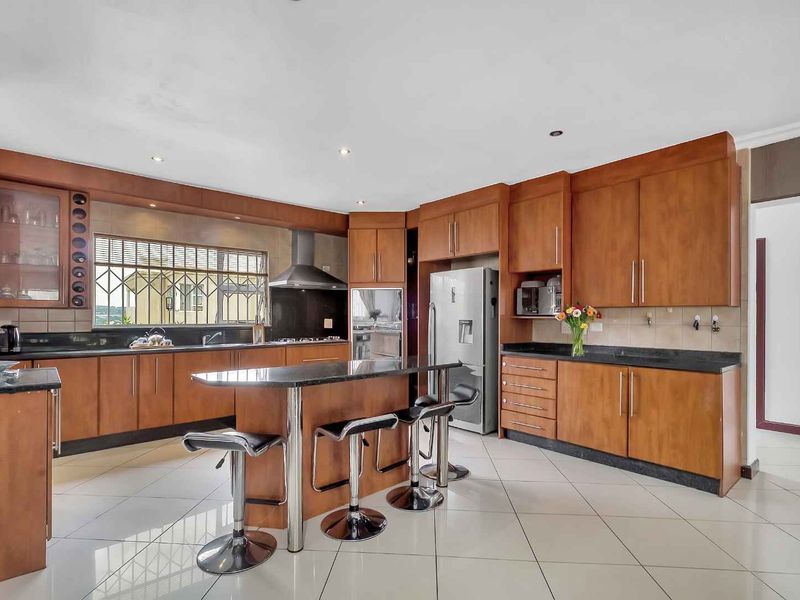 Spacious kitchen featuring warm-toned wooden cabinetry, granite countertops, a central island, and integrated stainless steel appliances with tiled flooring throughout.