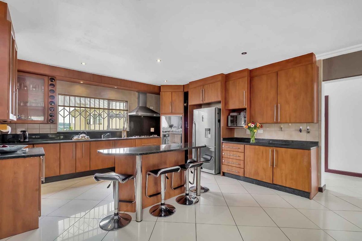 Spacious kitchen featuring warm-toned wooden cabinetry, granite countertops, a central island, and integrated stainless steel appliances with tiled flooring throughout.
