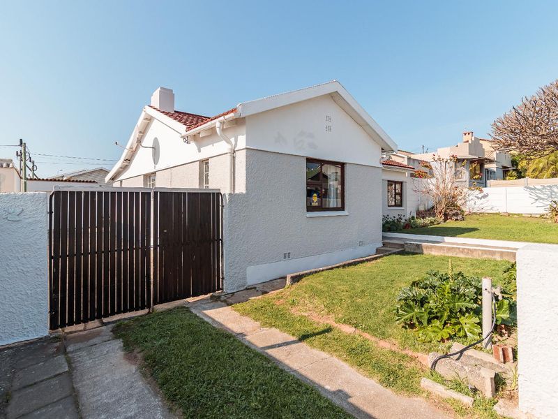Front view of a detached house featuring a tiled roof, chimney, timber gate, and a small front garden with a concrete driveway.
