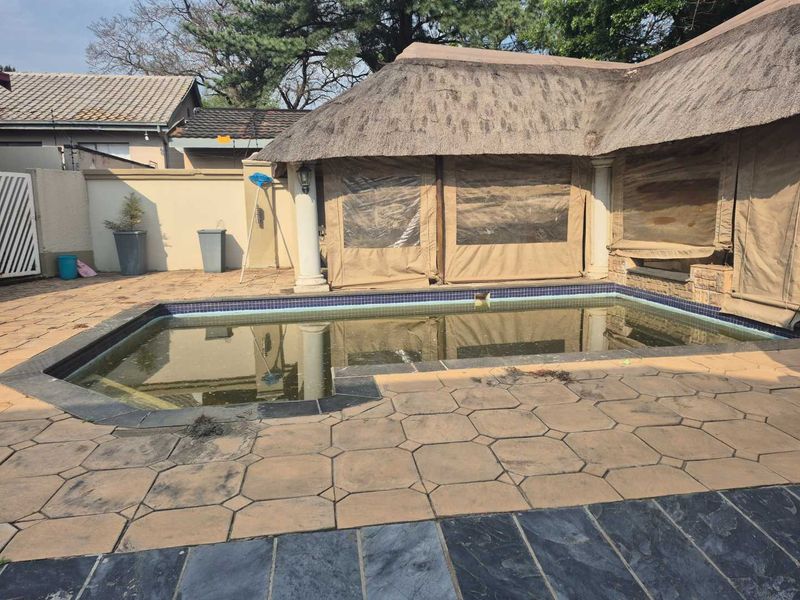 Outdoor pool area featuring a swimming pool, paved patio, and a covered entertainment space with a thatched roof.