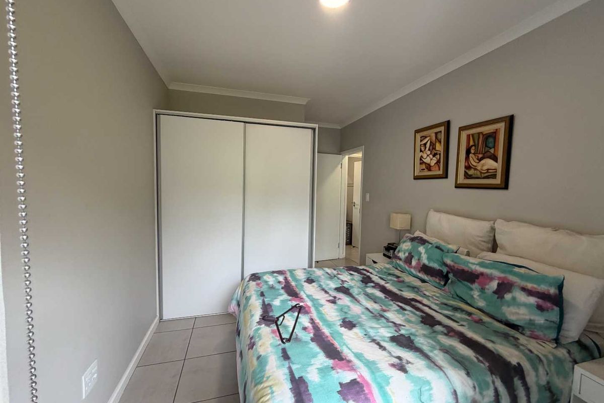 A well-maintained bedroom featuring neutral wall tones, tiled flooring, and a functional built-in wardrobe with sliding doors.