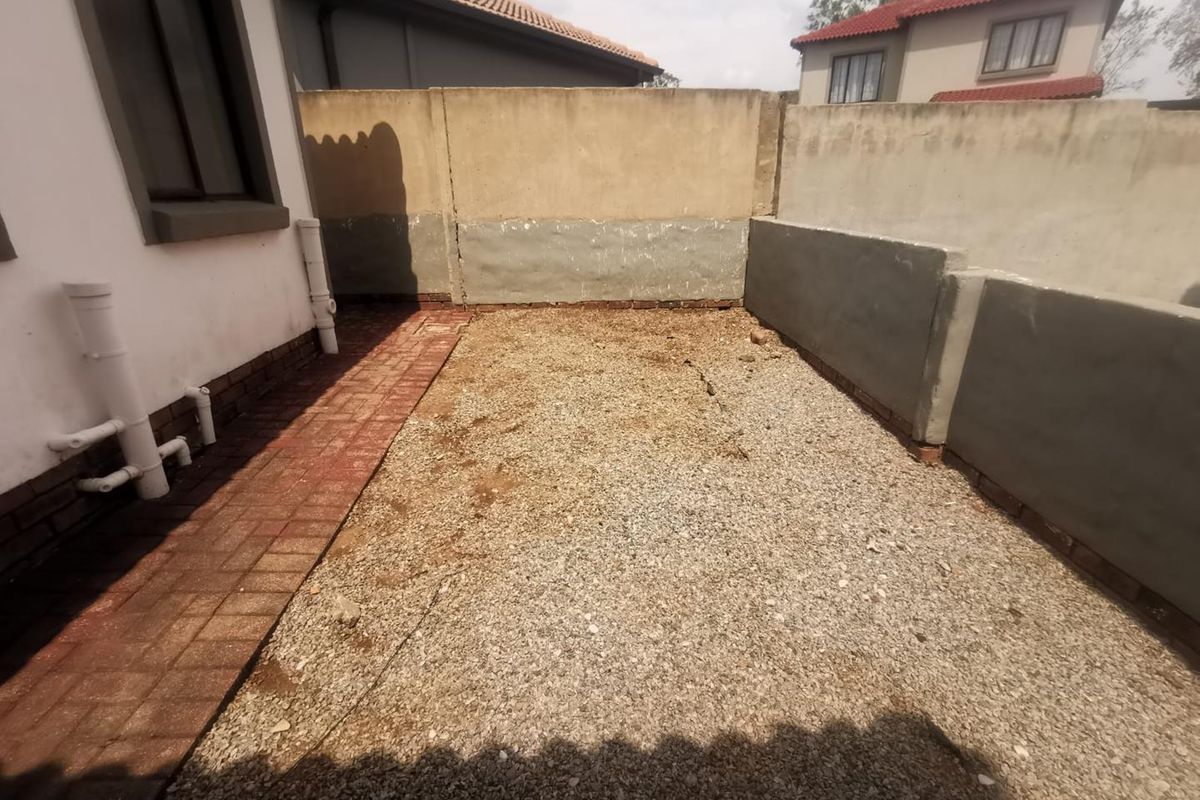 A rear exterior area featuring a gravel ground surface, paved walkway, and perimeter boundary walls with exposed plumbing fixtures.