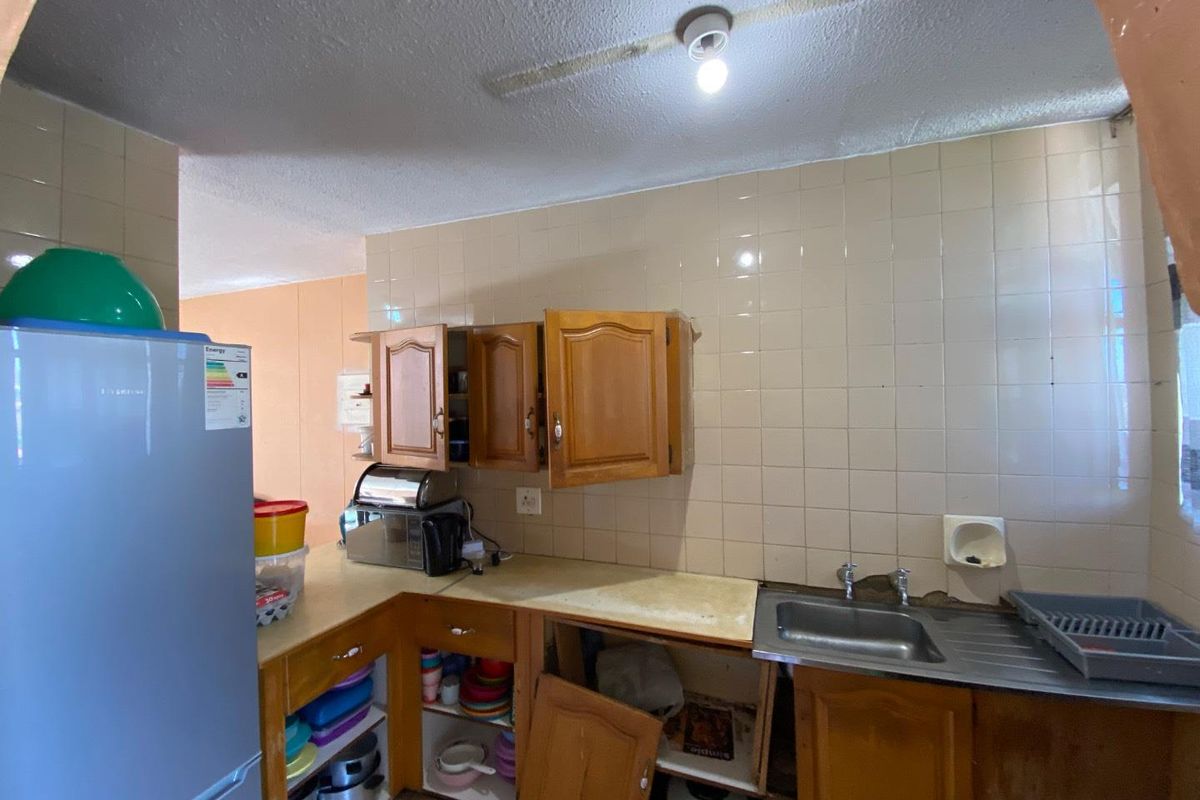 A dated kitchen featuring wooden cabinetry, a stainless steel sink, and tiled backsplash, currently showing signs of wear and maintenance requirements.