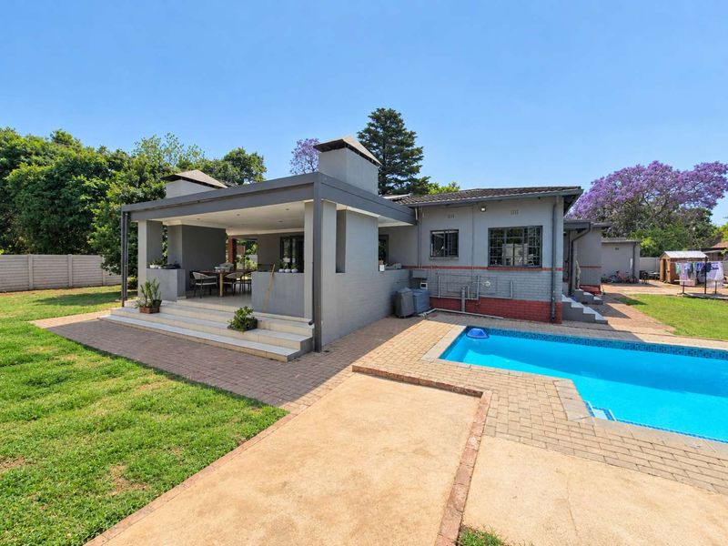 Rear view of the property featuring a covered patio with a built-in fireplace, a swimming pool, and a spacious garden area.