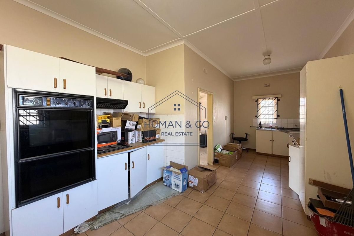 A dated kitchen featuring built-in oven, extractor fan, tiled flooring, and ample cabinetry, offering significant potential for modernization and renovation.