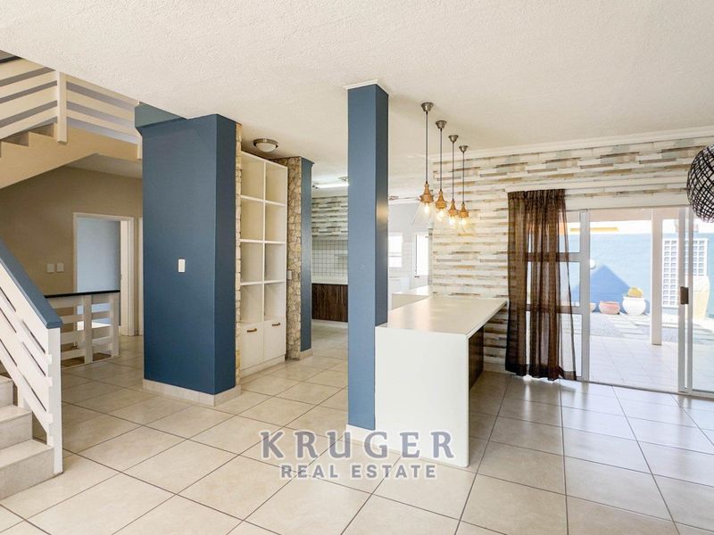 Spacious open-plan living area featuring a modern staircase, built-in shelving, breakfast bar, and direct access to the outdoor patio through sliding glass doors.