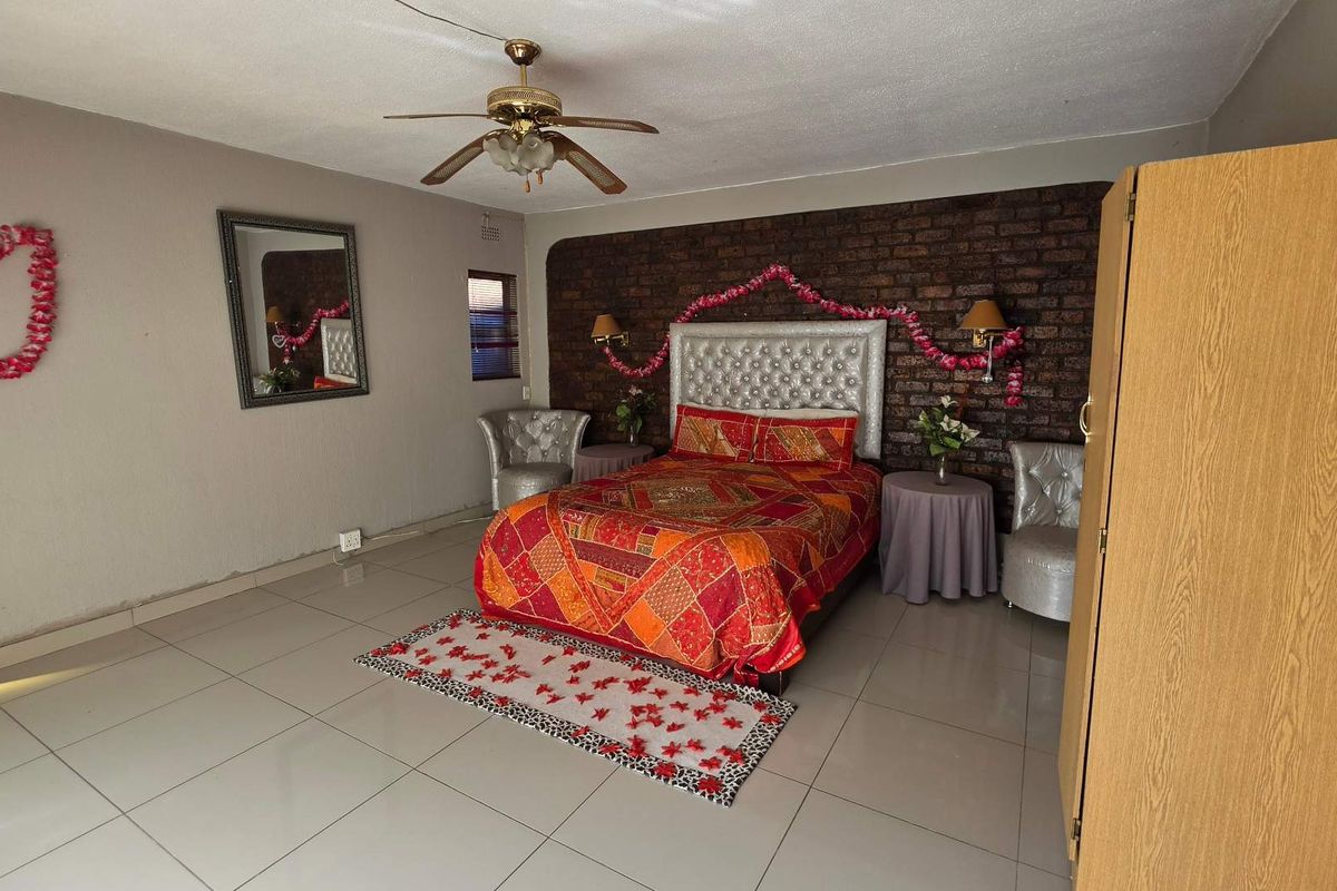 Spacious bedroom featuring a prominent exposed brick feature wall, neutral tiled flooring, and a ceiling fan.