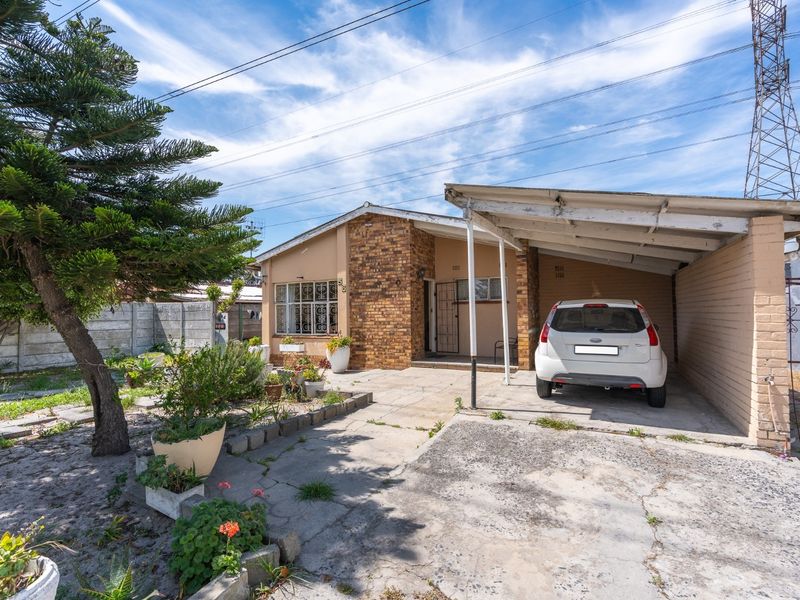 Front exterior view of a single-story brick house featuring a carport, concrete driveway, and established garden area.