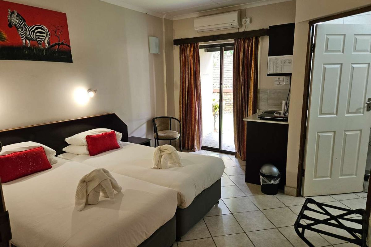 A lodge bedroom featuring twin beds, a small kitchenette area, tiled flooring, and sliding glass doors leading to an outdoor patio.
