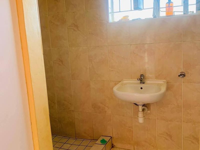 A functional bathroom featuring tiled walls and flooring, a wall-mounted basin, and a shower enclosure, currently requiring some maintenance and cosmetic updates.