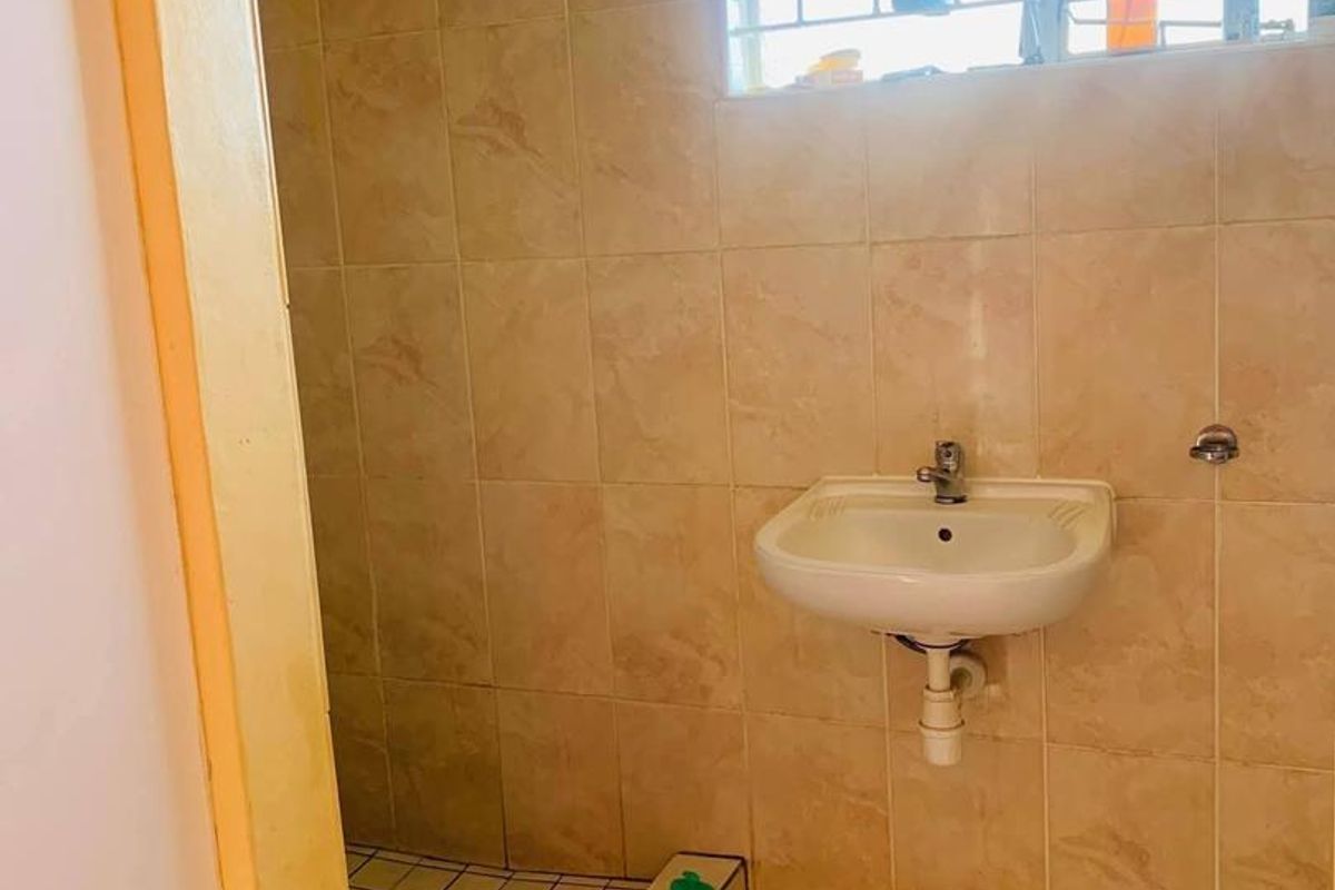 A functional bathroom featuring tiled walls and flooring, a wall-mounted basin, and a shower enclosure, currently requiring some maintenance and cosmetic updates.