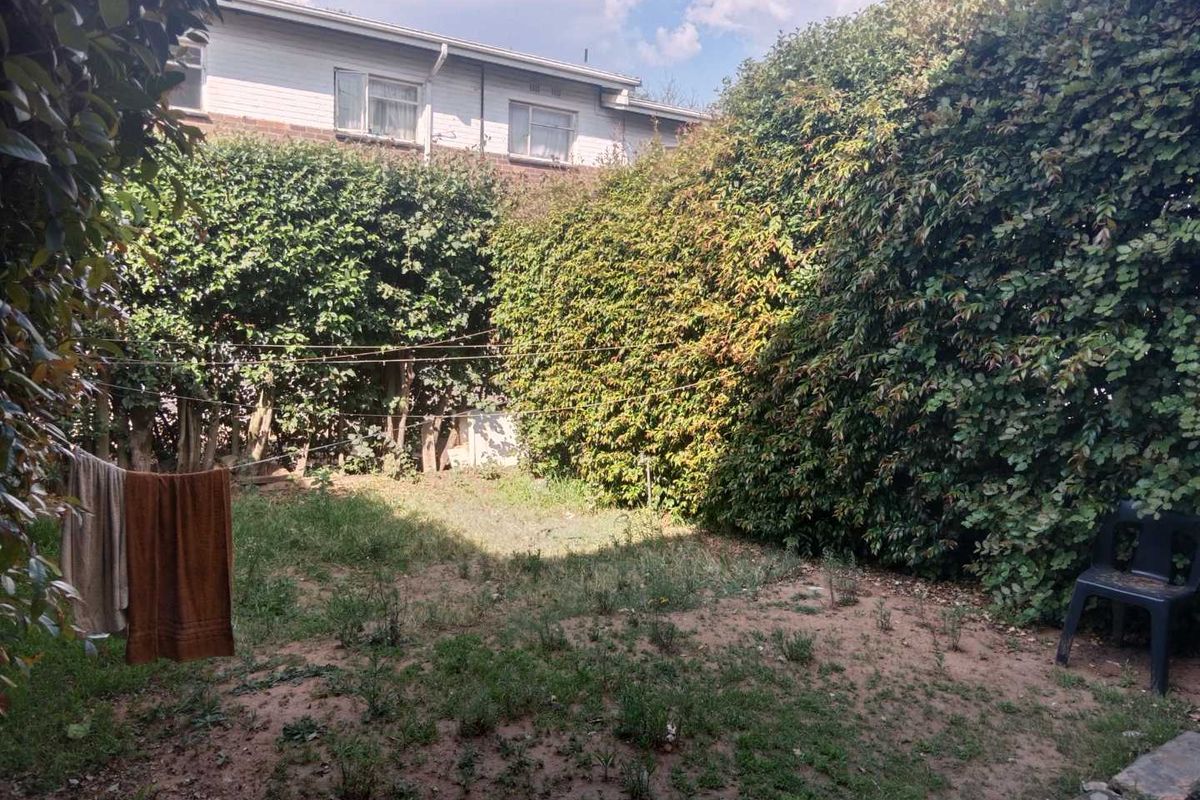 A private rear garden area featuring established perimeter hedges and a grass lawn, providing a secluded outdoor space for the apartment.